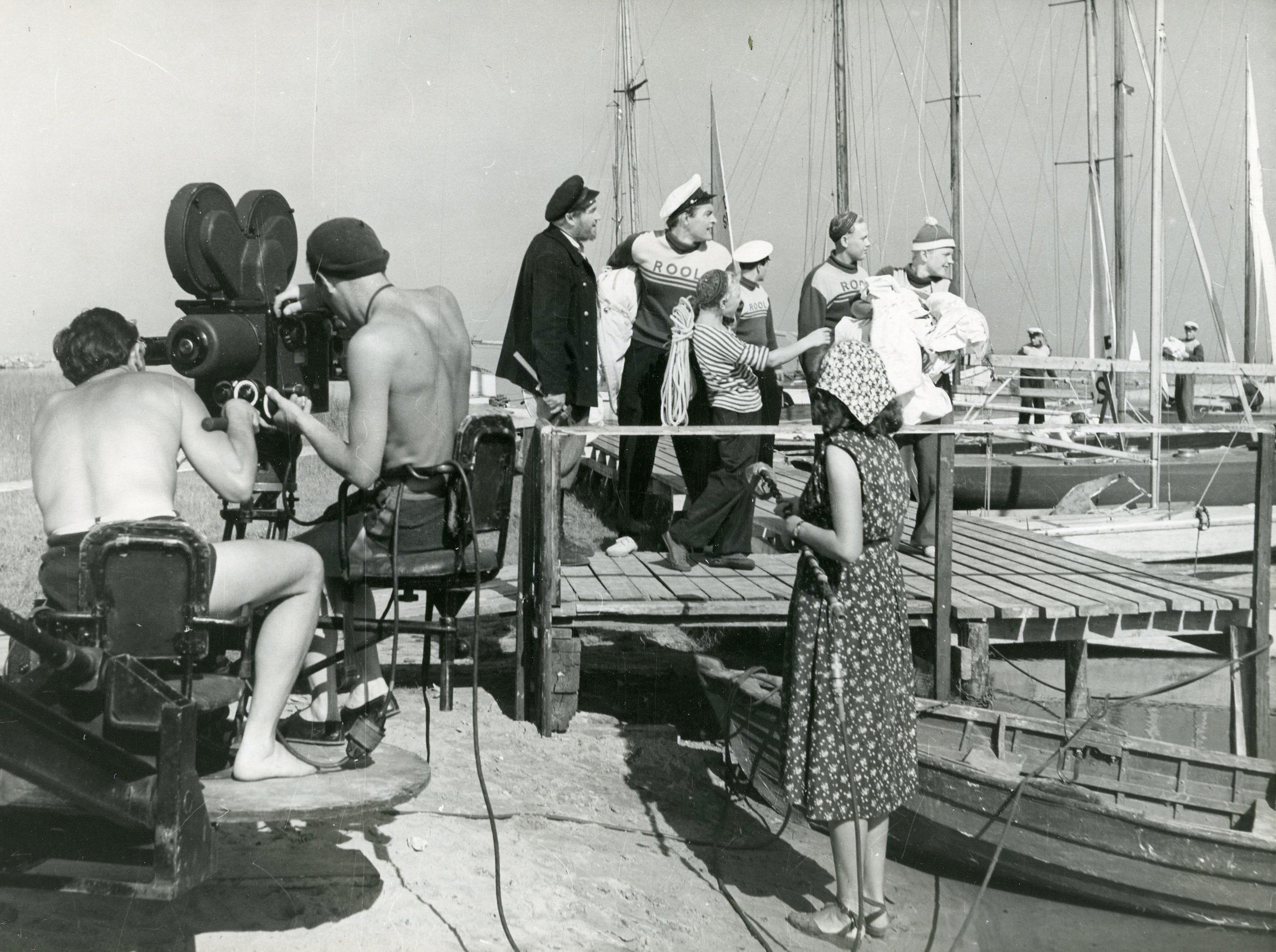 Filmivõtted Pirital (september 1955). Filmikaamera taga operaator Semjon Školnikov ja operaatori assistent Evald Vaher,  mikrofoniga seisab helioperaatori assistent, sadamasillal Peetri osatäitja Kaarel Karm, Juhani osatäitja Rein Aren ja poiste osatäitjad - Foto Armin Alla